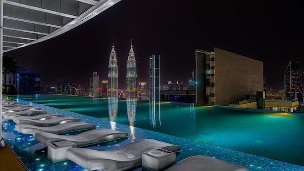 Une piscine moderne située sur le toit d’un bâtiment, offrant une vue sur les tours Petronas la nuit.
