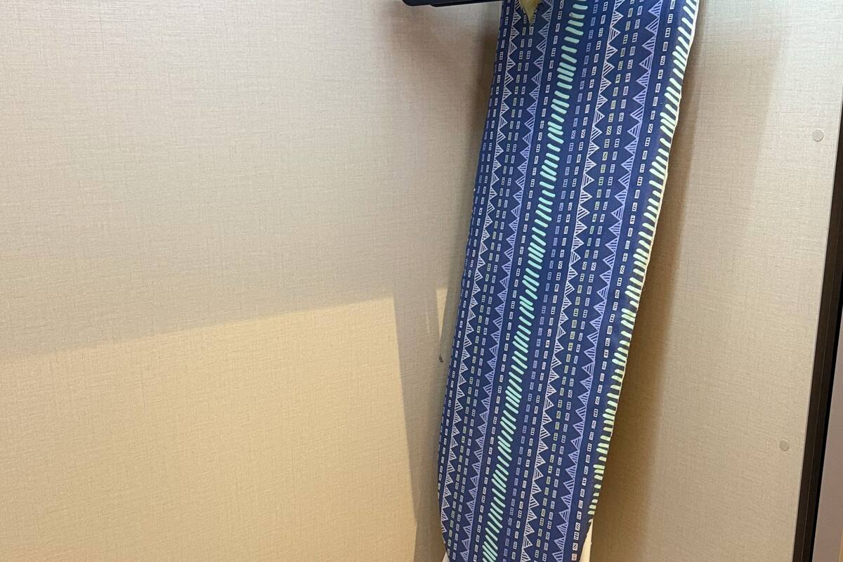 Een netjes georganiseerde werkruimte met een hangende kledingstuk, een paar schoenen en een draagbaar strijkijzer op een houten oppervlak.