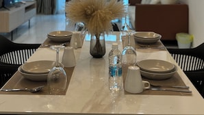 Un coin repas avec une table dressée pour quatre personnes, un vase contenant des fleurs séchées et un lustre moderne.