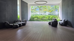 Un salon moderne doté d’un plancher en bois, de murs sombres et offrant une vue sur la verdure et les bâtiments.