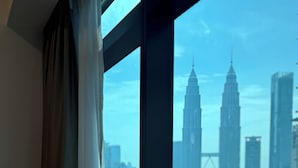 Une vue sur un paysage urbain à travers une fenêtre ornée de rideaux, avec de grands bâtiments, dont les tours Petronas.