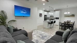 A modern living room with a flat-screen TV, grey sofas, and a dining area with a kitchen in the background. - Peaceful 2-bedroom townhome -Sleeps 6 in La Feria (La Feria)
