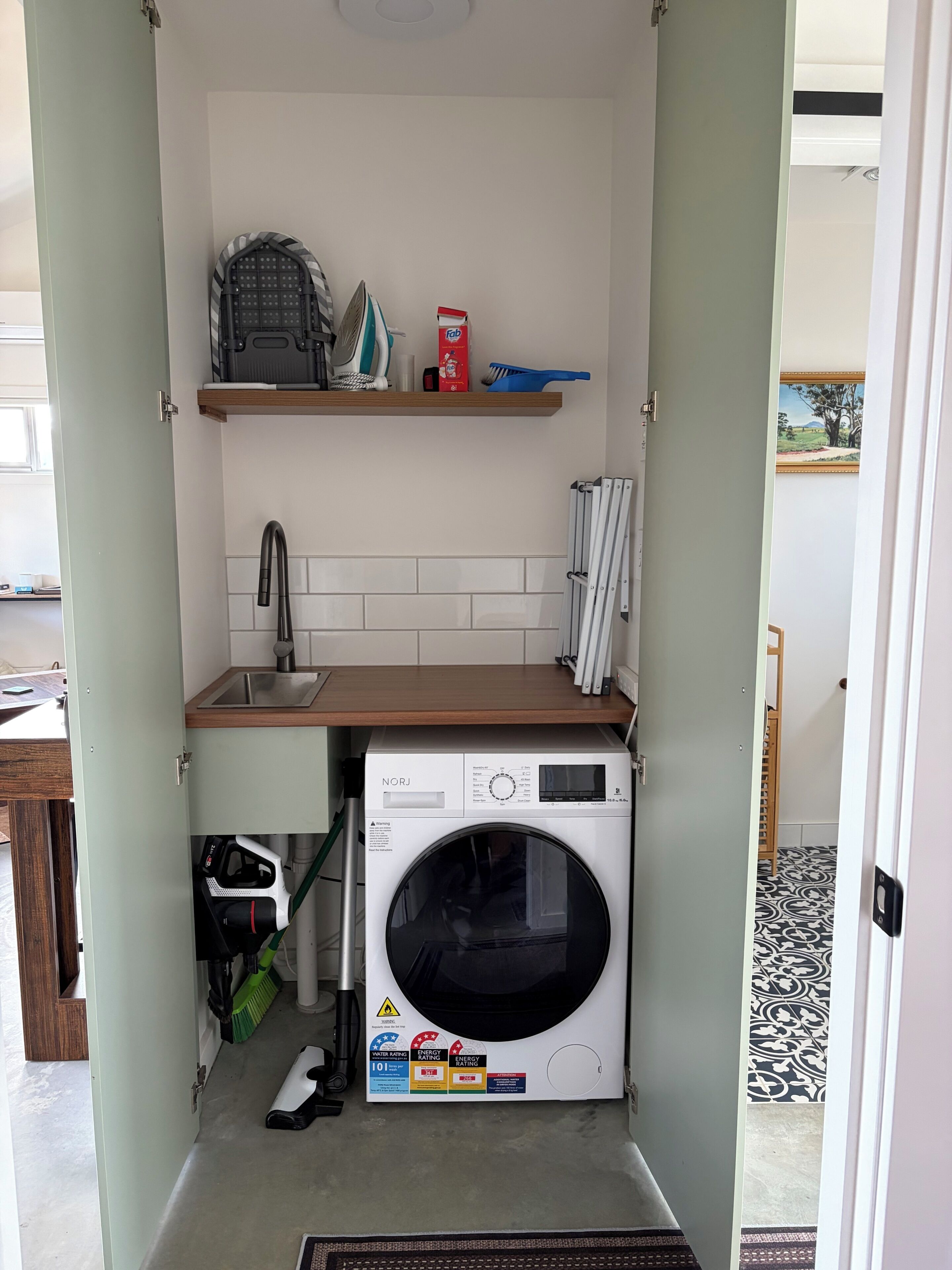 Ein kleiner Hauswirtschaftsraum mit Waschmaschine, Spüle und Ablage für Reinigungsmittel.