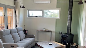 Ein modernes Wohnzimmer mit einem grauen Ecksofa, einem Holztisch, einem Kamin und einem großen Fenster, das für natürliches Licht sorgt.