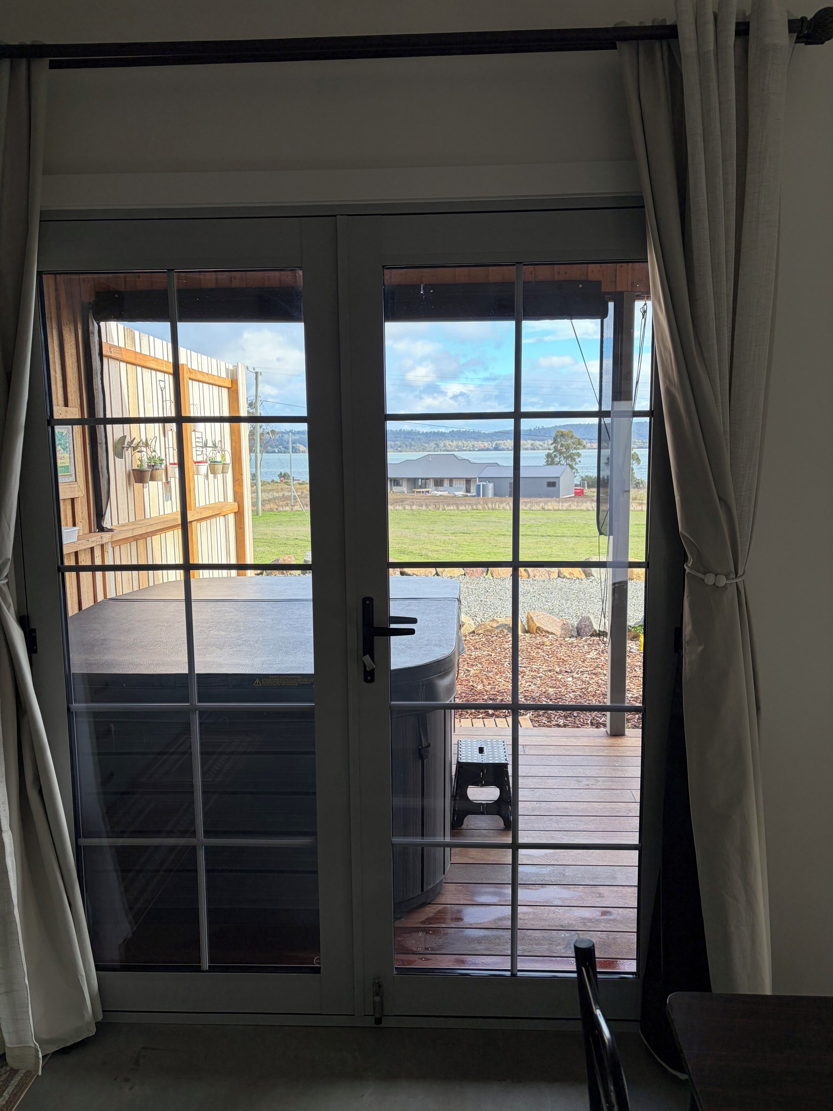 Porta de correr de vidro que dá para um deck externo, com vista para uma área gramada e um corpo d'água.
