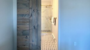 Eine schiebetür im Barbürgertum-Stil führt zu einem Badezimmer mit Dusche und Fliesenboden.