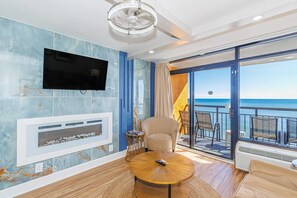 A room with a flat-screen TV, a fireplace, a round coffee table, and a balcony with outdoor seating. - Landmark 1036 (Myrtle Beach)