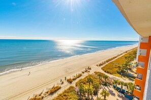 Blick auf einen Strand von einem Balkon mit Blick auf einen Sandstrand, einen klaren Himmel und den Ozean.