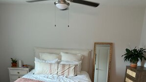 Un dormitorio con cama, mesita de noche, cómoda, ventilador de techo y una puerta.