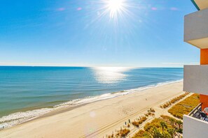 A beach view from a balcony with a clear sky and sun shining over the ocean. - Landmark 1430 (Myrtle Beach)