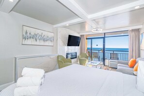 A hotel room with a bed, a flat-screen TV, a painting, a balcony with a view of the sea, and a seating area with chairs. - Landmark 1430 (Myrtle Beach)