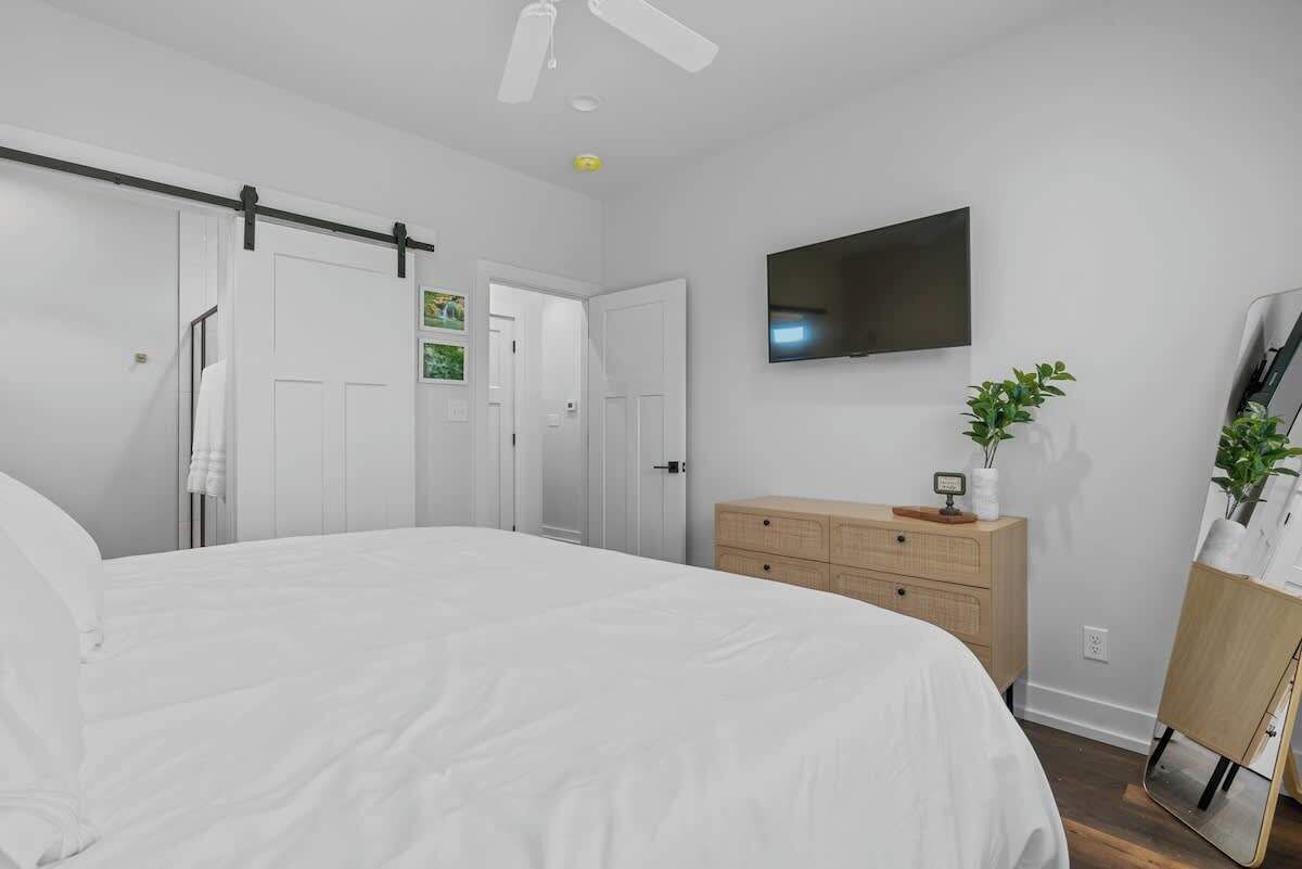 A bedroom with a bed, a dresser, a TV mounted on the wall, and a sliding door.