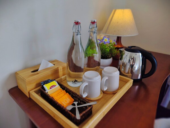 A wooden tray with a tissue box, two bottles, a mug, a spoon, and a packet of sugar.