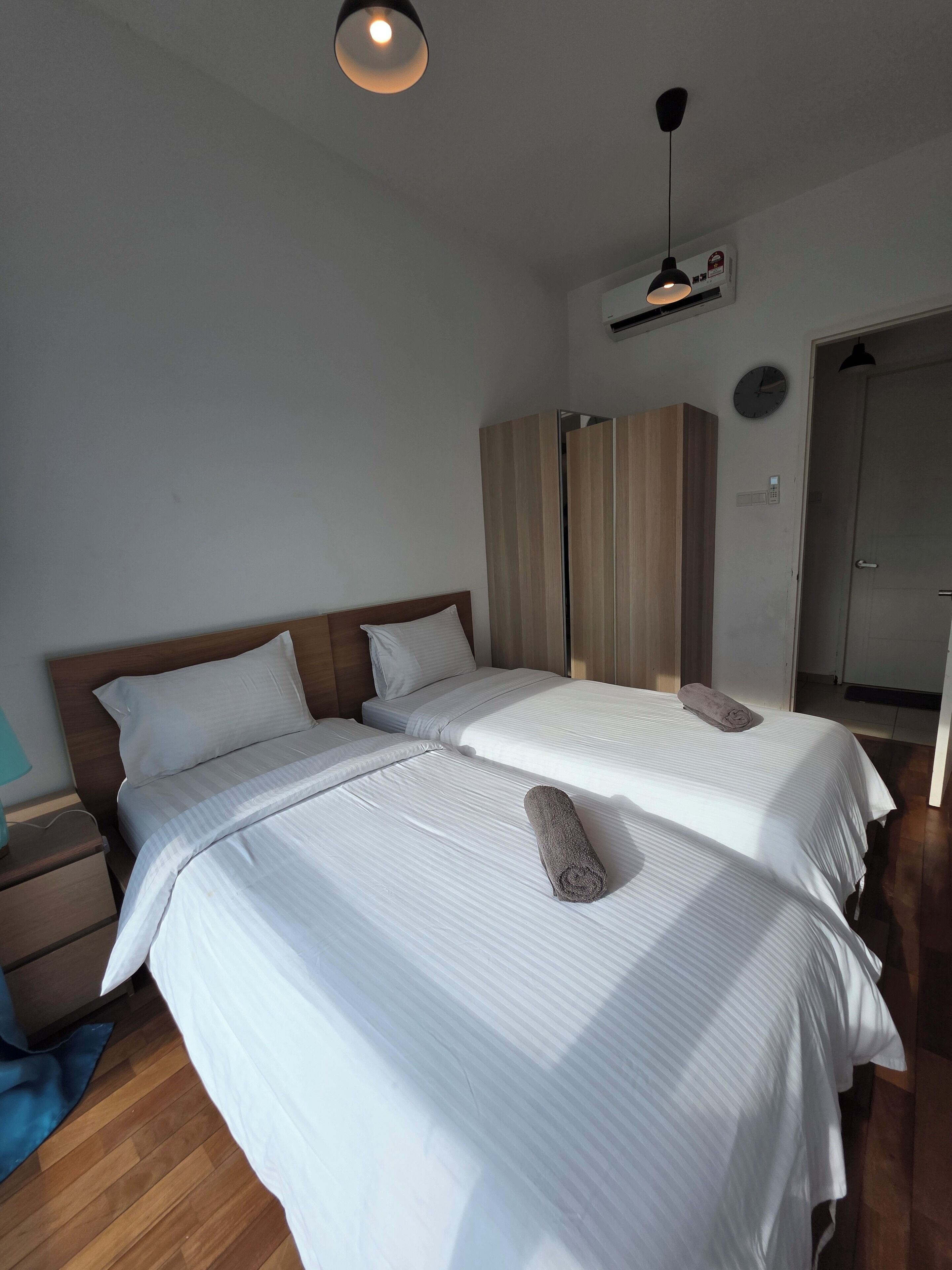 A double bed with white bedding and a wooden headboard, a bedside table with a lamp, and a wardrobe with vertical stripes.