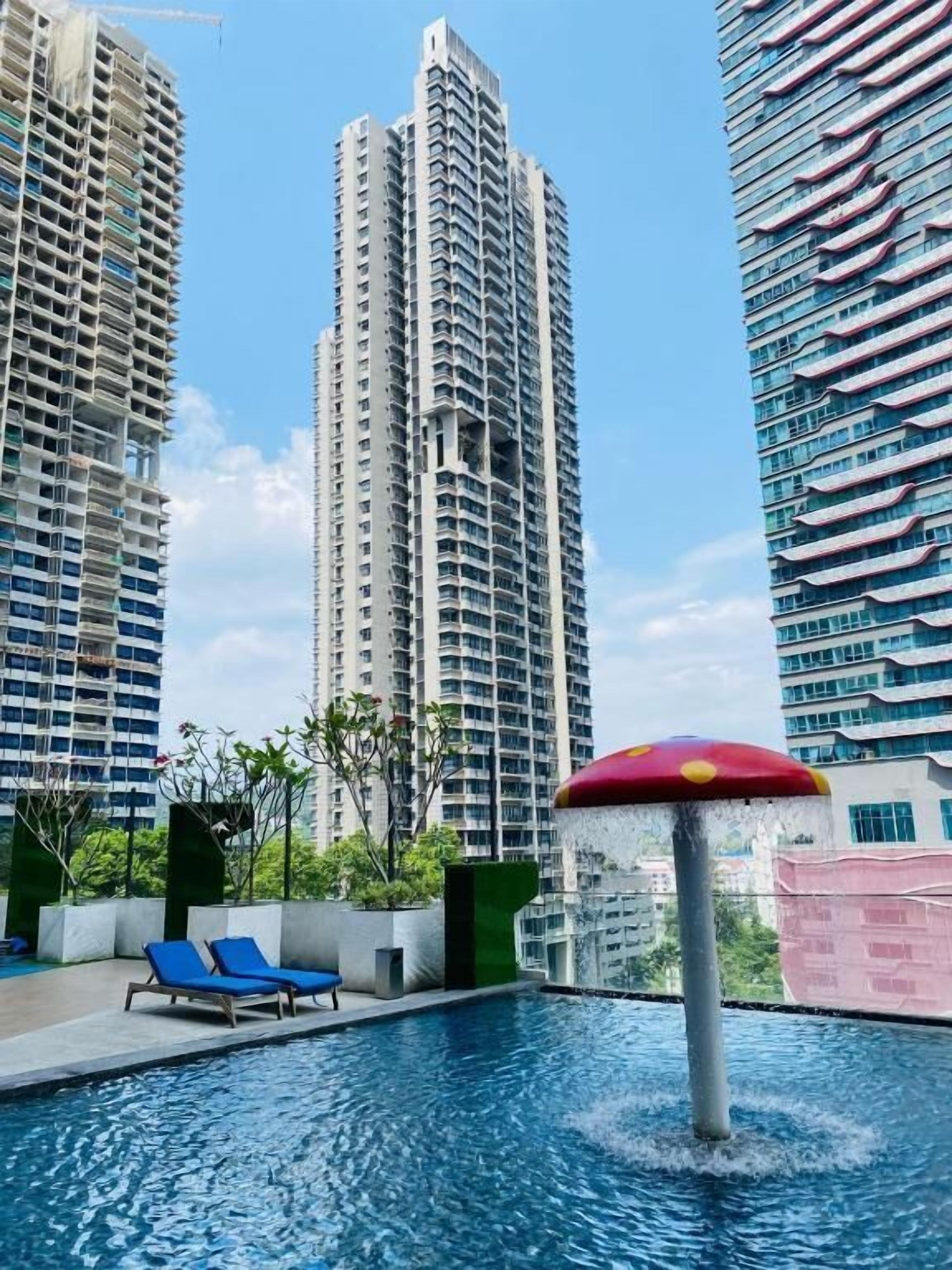A swimming pool with lounge chairs and a decorative umbrella, surrounded by high-rise buildings.