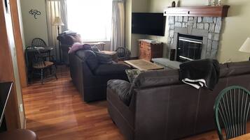 Un salon avec une cheminée, un téléviseur et un coin repas comprenant des chaises et une table.