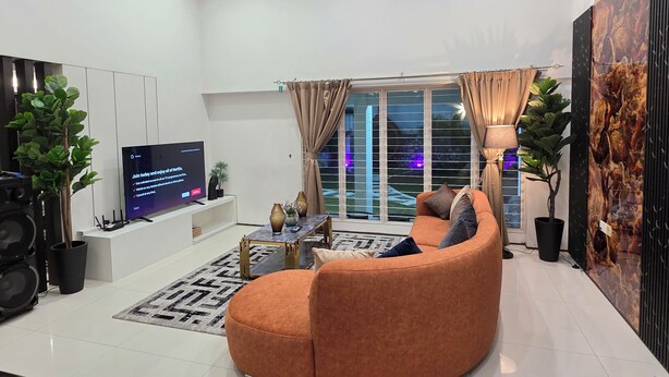 Ein modernes Wohnzimmer mit einem gewölbten, orangefarbenen Sofa, einem Flachbildfernseher, einem Couchtisch und einem großen Fenster mit Vorhängen.