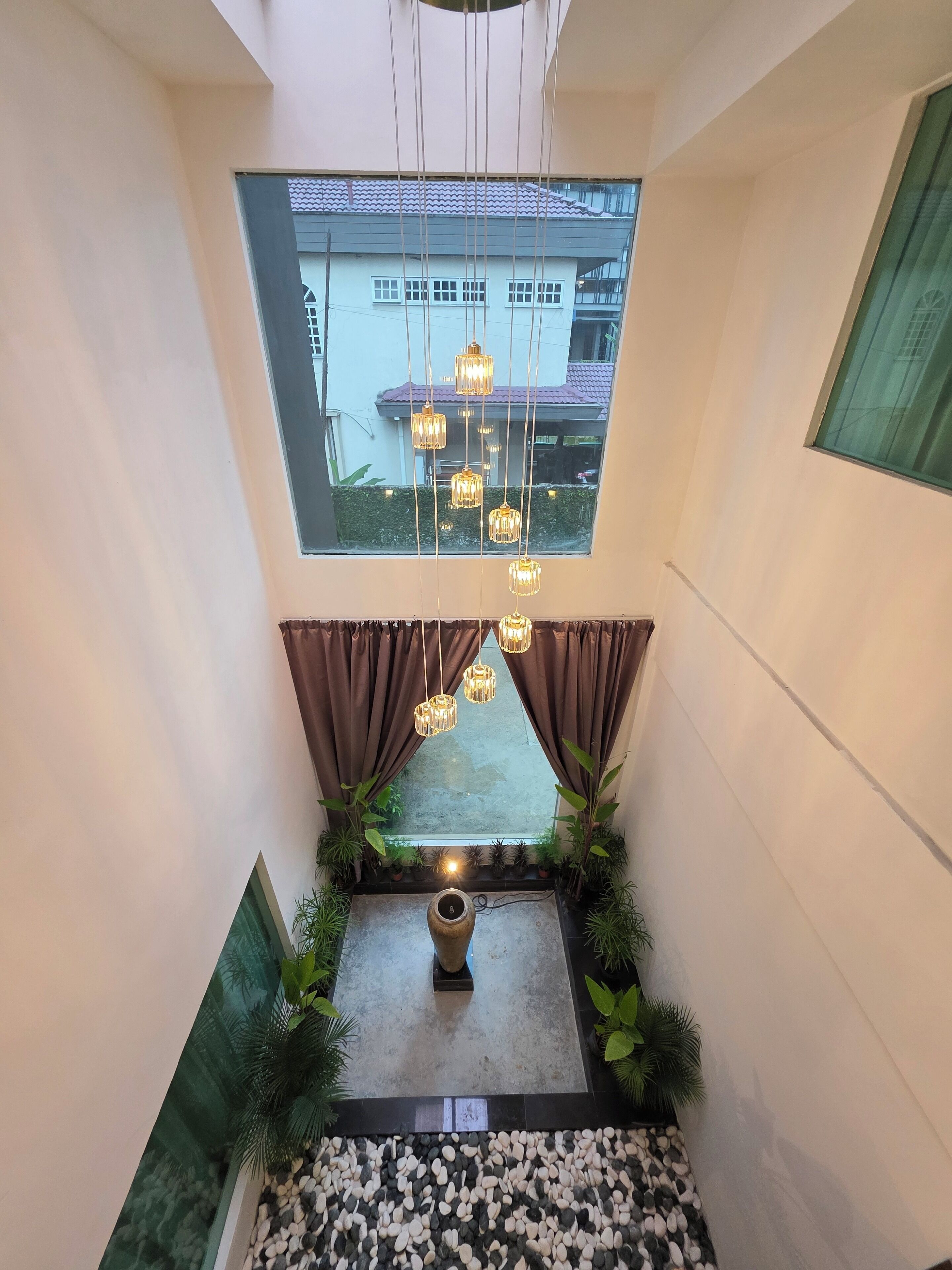 Un interior moderno con tragaluces, lámparas colgantes, una planta central y un elemento decorativo de piedra.