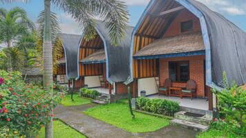 Un hotel de estilo bungalow con techos de paja y vigas de madera, que cuenta con un patio con mobiliario exterior y abundante vegetación.