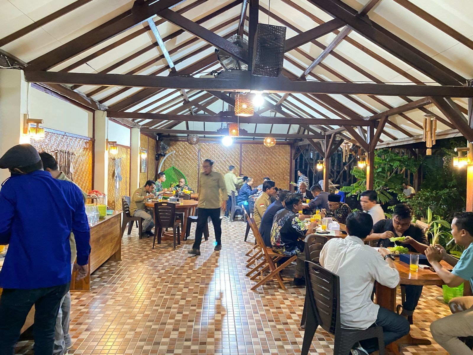 A restaurant with a tiled floor and wooden beams on the ceiling. Tables are arranged for dining, and people are seated.