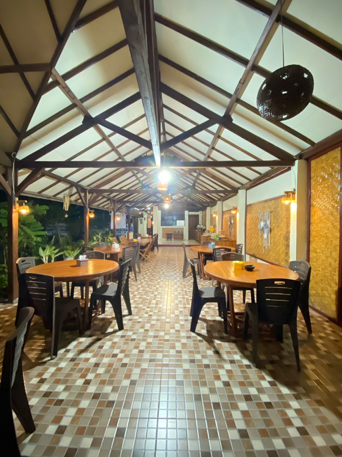 Un espacio de comedor al aire libre techado, con suelo de baldosas, mesas y sillas de madera.