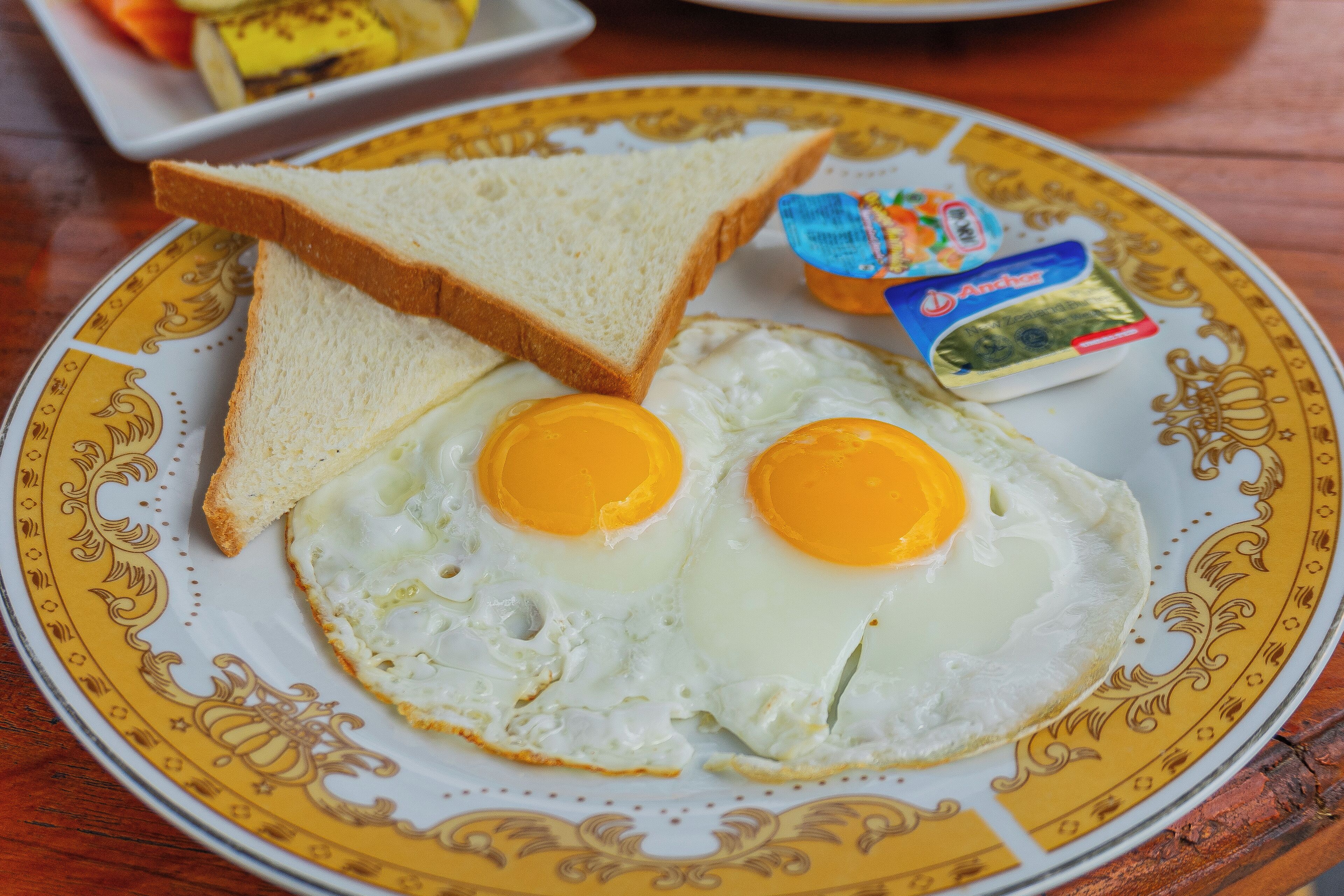 Une assiette décorative sur laquelle on trouve deux œufs au plat, une tranche de pain grillé et un petit paquet de beurre.