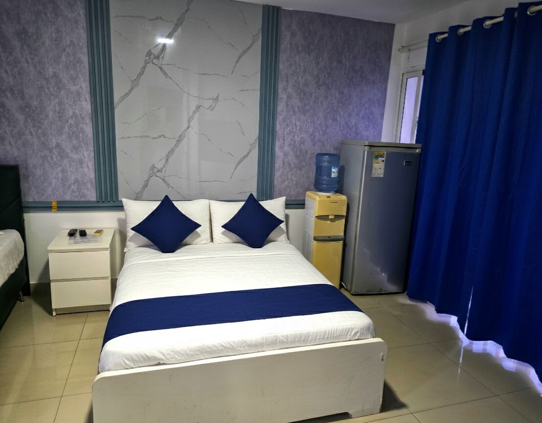 Een hotelkamer met een bed, nachtkastje, waterdispenser en een koelkast.