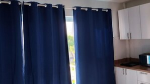 Una cocina con armarios blancos, encimera negra y ventana con cortinas azules.