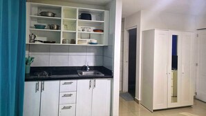 Una cocina con armarios blancos, una encimera negra y un fregadero de acero inoxidable. Se observa una cortina azul a la izquierda y un armario blanco a la derecha.