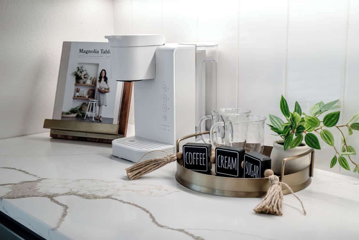 Une machine à café, un porte-tasse et une plante en pot sur un plan de travail de cuisine.