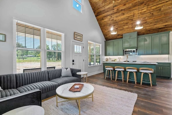 A modern kitchen with green cabinets, a bar area with stools, and a large window overlooking a garden.