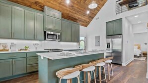 Een moderne keuken met groene kasten, een centraal eiland met krukken en een houten plafond.
