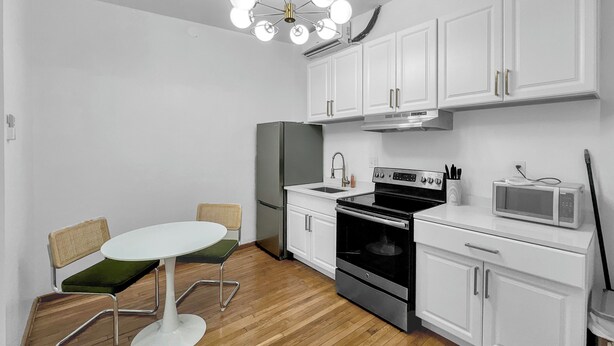 Une cuisine moderne avec des meubles blancs, une cuisinière noire, un four à micro-ondes et un coin repas comprenant une table et des chaises blanches.