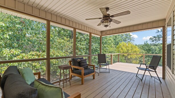 Una terrazza coperta all'aperto con mobili in legno, una ventola a soffitto e vista sugli alberi.