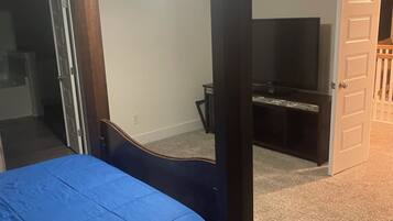 A bedroom with a four-poster bed, a ceiling fan, a television, and a door leading to another room.