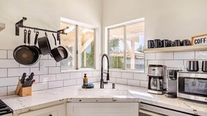 Een moderne keuken met witte kasten, een roestvrijstalen fornuis, een koffiehoek en een raam dat natuurlijk licht binnenlaat.