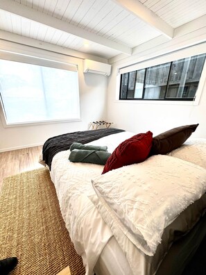 A bedroom with a large window, a bed with multiple pillows, a small table, and a hanging light fixture. - Little Red Gate Urban Retreat (Kingston)