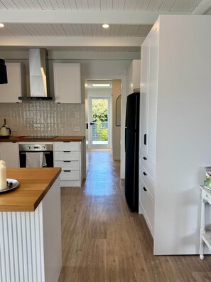 Eine moderne Küche mit weißen Schränken, einer Holz Arbeitsplatte, einem schwarzen Kühlschrank und Blick auf einen Balkon.