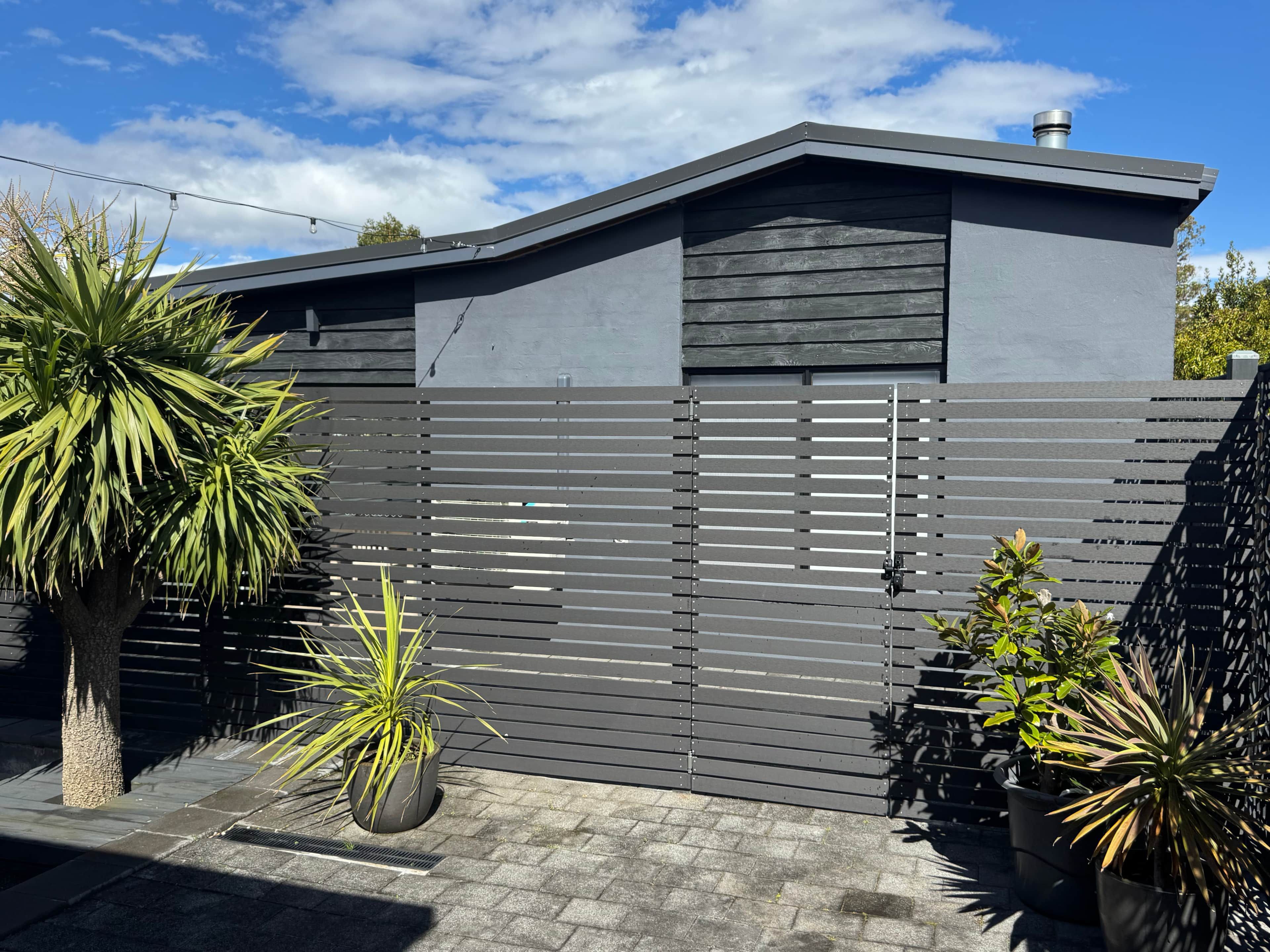 A modern building with a grey exterior, a sloped roof, and a metal gate.