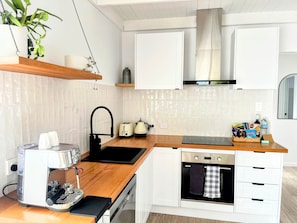 A modern kitchen with white cabinets, a wooden countertop, a built-in oven, a coffee machine, and a hanging plant. - Little Red Gate Urban Retreat (Kingston)