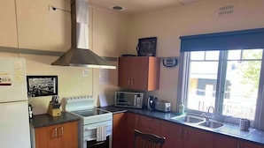 A compact kitchen with a stove, microwave, sink, and wooden table. - The Cottage at Raheen (Mallacoota)
