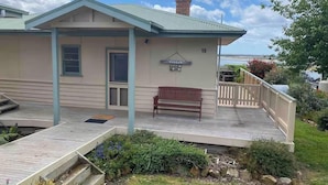 A house with a covered porch, a bench, and a number 19 sign. - The Cottage at Raheen (Mallacoota)
