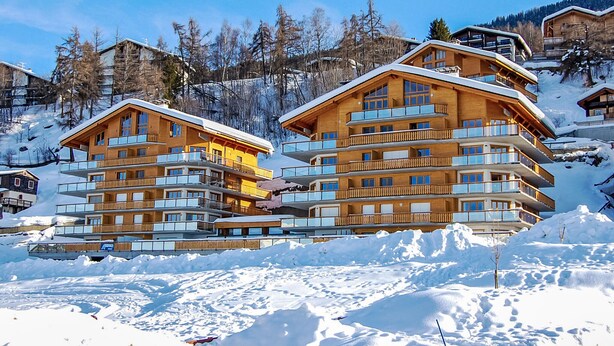 A multi-story wooden lodge with balconies, surrounded by snow-covered terrain and trees. - Domaine des Reines D10 by Interhome (Nendaz)