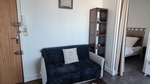 Une petite pièce agréable et chaleureuse, avec un canapé gris, une porte en bois, un petit miroir fixé au mur et une bibliothèque.