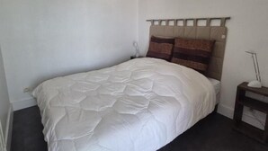 Un lit simple avec une couette blanche, une tête de lit à panneaux multiples et une table de chevet avec une lampe.