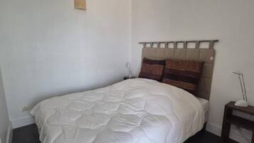 Un lit simple avec une couette blanche, une tête de lit à panneaux multiples et une table de chevet avec une lampe.