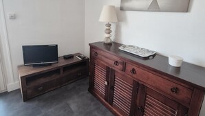 Une pièce avec un téléviseur posé sur un meuble en bois, une lampe, une petite table avec un plateau et un tableau accroché au mur.
