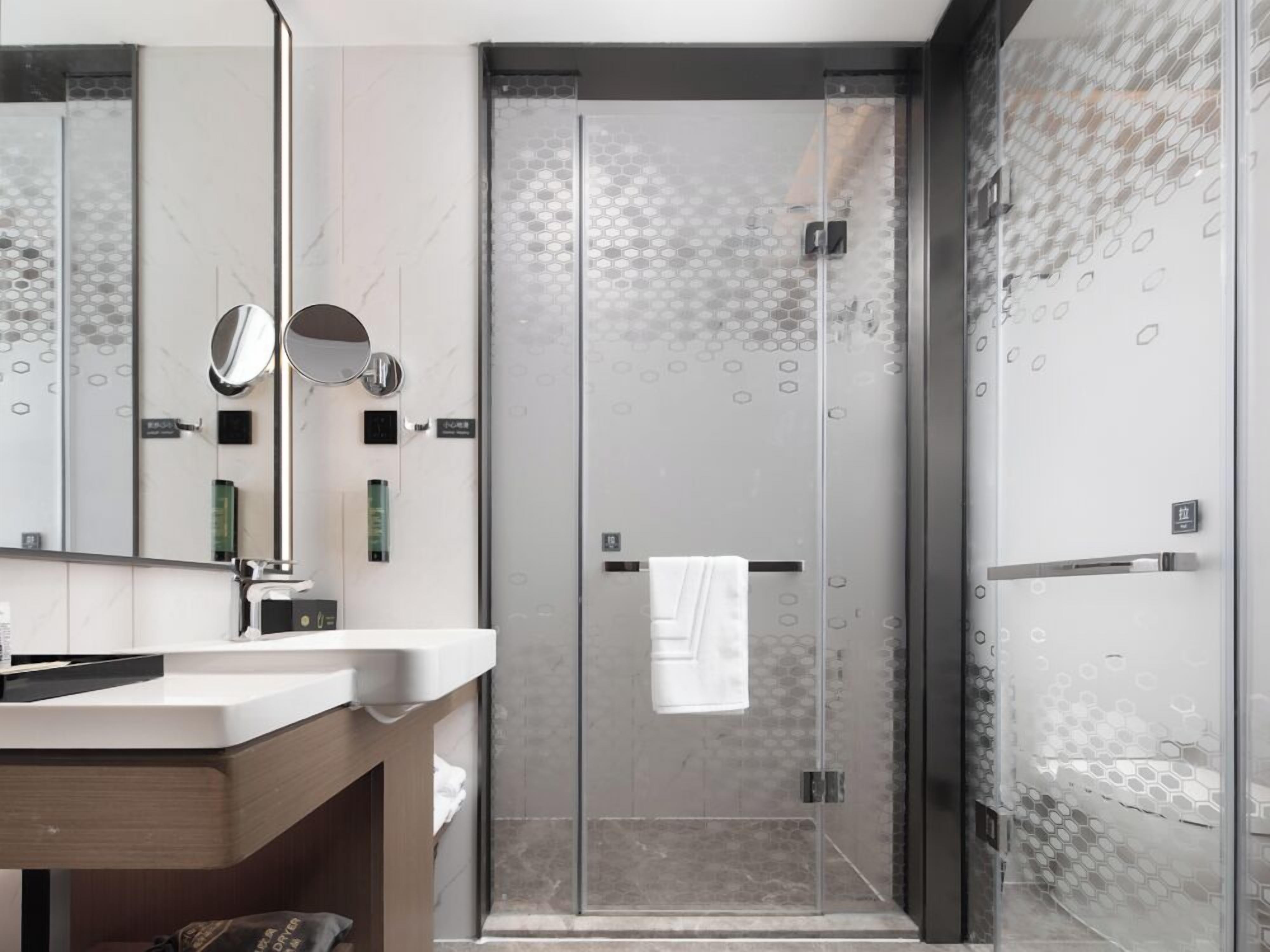A modern bathroom with a glass-enclosed shower, a vanity with a mirror, and a towel hanging on the door.