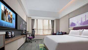 Una habitación de hotel moderna con una cama grande, un escritorio con computadora, un televisor montado en la pared y una ventana con cortinas.