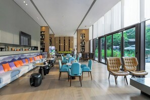A modern interior with a sofa, chairs, tables, and a TV. - Hampton by Hilton Emeishan Scenic Area (Leshan)